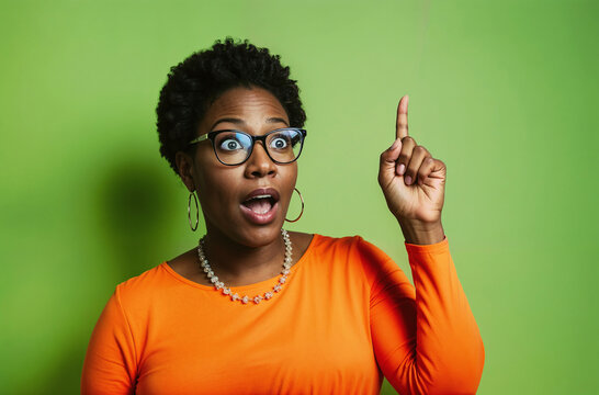 African American woman pointing finger up with a surprized facial expression, isolated on a green background
