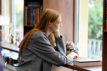 in bookstore near the window a beautiful student is sitting reading books preparing for exams...