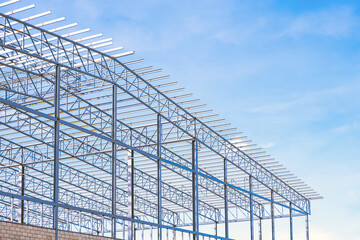 Metal roof beam and columns of large industrial factory building structure in construction site against blue sky background, low angle and perspective side view