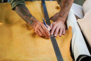 Closeup and crop hands of leather craftsman using a pencil and steel ruler drawing design on the yellow leather in the workshop.