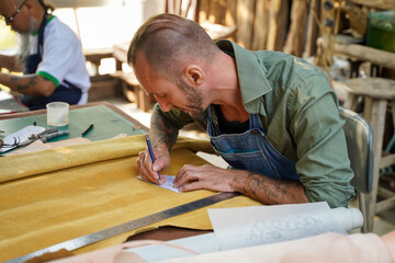 Leather craftsman using a pencil drawing draft design on the yellow leather in the workshop.