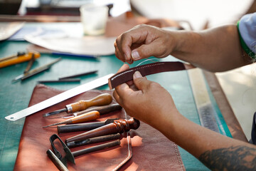 Closeup and crop hands of leather craftsman with his tool intend sewing and repair leather brown bag for a customer in workshop .