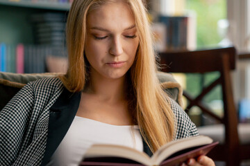 close up in a beautiful bookstore a young girl with long hair sitting in a chair reads a book...