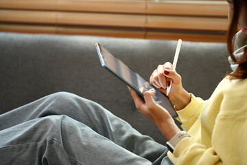 Portrait of pretty asian female using digital tablet sitting on couch at home