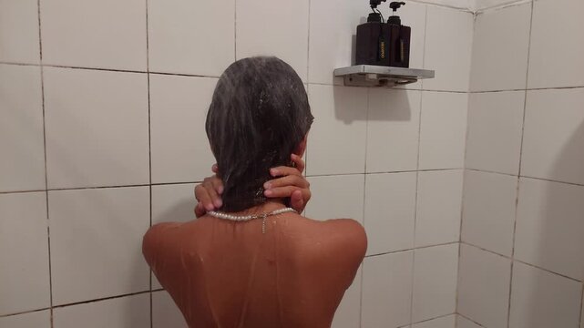 Young woman showering. Shampoo and shower gel in the background with no logo.
