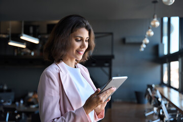 Young latin Hispanic adult professional business woman looking at online trade app. European mature businesswoman CEO holding digital tablet using fintech tab application working in workspace office