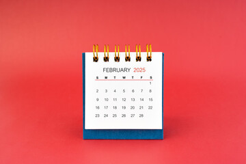 February 2025 white desk calendar on red background.