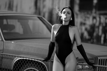 Beautiful sexy women vaping outdoor. Fashion model sitting near retro car and smokes electronic...