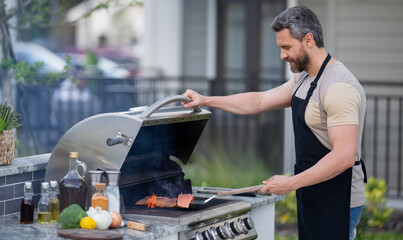 Hispanic man cooking on barbecue in the backyard. Chef preparing barbecue. Barbecue chef master. Man in apron preparing delicious grilled barbecue food, bbq meat. Grill and barbeque.