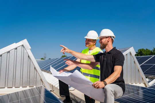 Two solar technicians discussing installation plan on the rooftop of a company building with solar panels.