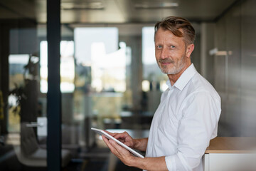Smiling senior businessman with tablet PC at office
