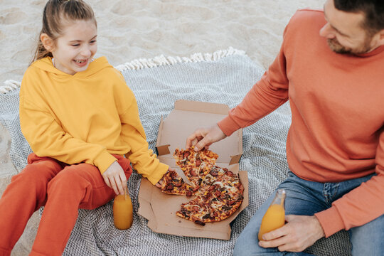 Father and daughter eating pizza sitting at beach