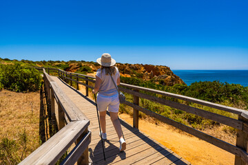 Summer vacation in Lagos Portugal. Young woman in beige casual clothes and sun hat practicing...
