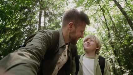 Handheld POV shot of Caucasian father and son recording lifestyle video blog while having family hiking trip in forest on sunny day