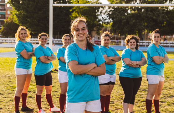 Smiling rugby players standing with arms crossed at field on sunny day