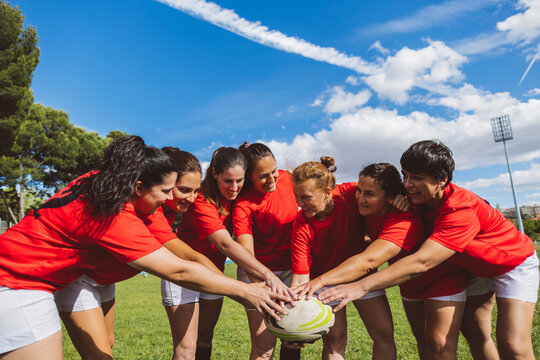Happy rugby players holding ball together under sky at field