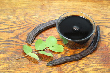Carob Molasses and locust beans on wooden background	