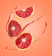Juice splashes and fresh red oranges in air on coral color background