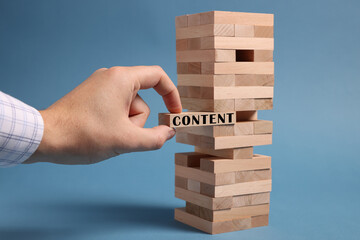 Man removing wooden block with Content from tower on light blue background, closeup