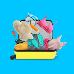 Different beach stuff falling into suitcase on light blue background