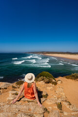 Viewpoint on portuguese beach bordeira praia. Beautiful woman with long blonde hair wearing orange...
