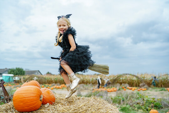 Girl wearing bat costume flying on broomstick in pumpkin patch