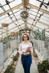 Small greenhouse business. Businesswoman selling flowers and seedlings, standing in greenhouse, looking at camera, smiling.