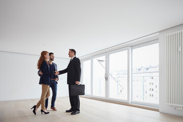 Young couple buying real estate apartment and closing deal with handshake