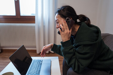 Young woman multitasking with phone and laptop at home