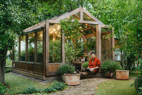 Businessman sitting with laptop at greenhouse in back yard