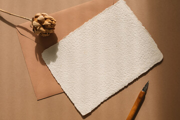 Overhead view of blank piece of homemade deckle edge card, envelope, a calligraphy pen and a dried...