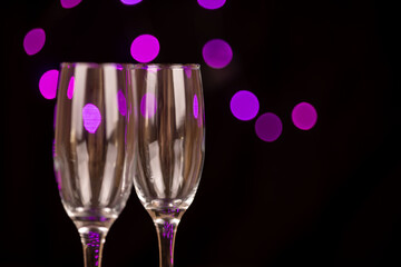 Detailed view of empty champagne glasses on a black background with violet bokeh lights. A sophisticated touch for holiday parties and New Year's celebrations.