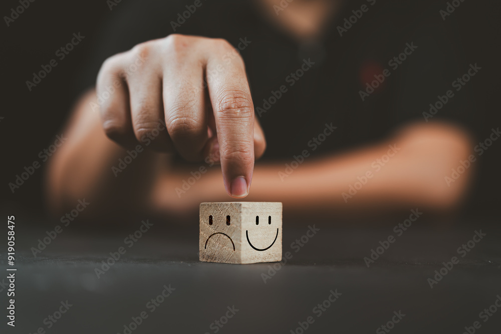Wall mural man hand points on a wooden cube with happy smile face on bright side and unhappy face on dark side 