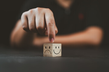 Man hand points on a wooden cube with happy smile face on bright side and unhappy face on dark side...