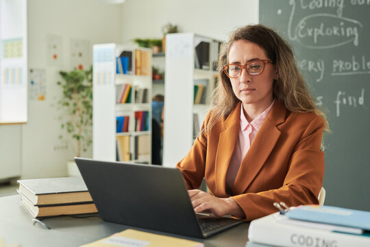 Portrait of adult woman as female teacher using laptop at desk while working in school library copy space