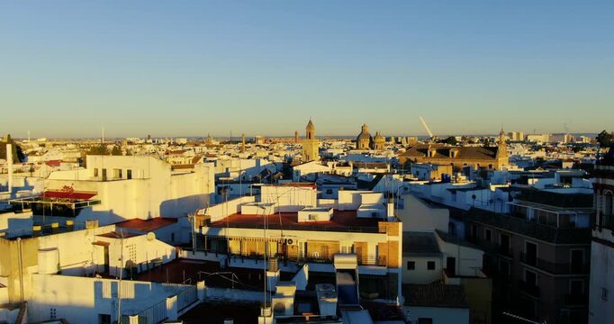 Ascending aerial footage in the historic center of Seville, where you can see the rooftops and churches with the orange color of the sunset.
