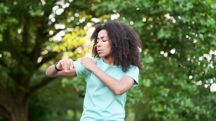 Young athletic african american female suffers from sharp pain in her shoulder during a jog workout in urban city park. Black woman was injured. Unfortunate athlete rubs massages muscles on sore spot