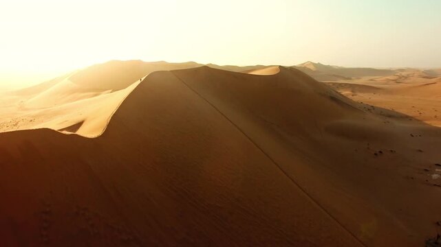 Hiking, exploring and adventure with a man walking on a sand dune in a hot, arid and barren desert landscape. Drone of a hiker on a journey of discovery and freedom while traveling through Africa