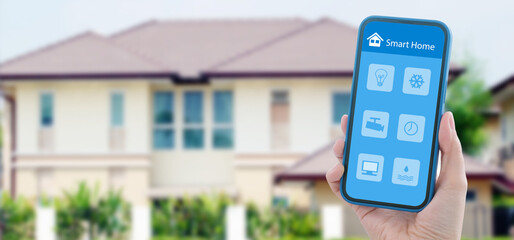 Hand using mobile phone for smart home automation control app over blur house background, Wireless...