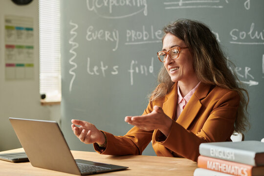 Side view portrait of smiling female teacher talking to video chat during online lesson with student and gesturing