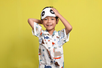 Portrait of cute Asian boy wearing pajamas and sleep mask isolated on yellow background. Healthy sleep concept. Copy space