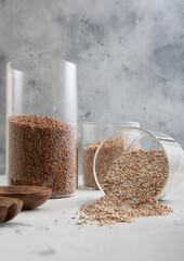 Brown and green dry raw organic buckwheat seeds in glass jar on light kitchen table.Macro.
