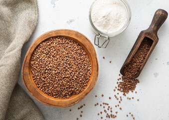 Bowl of brown dry raw organic buckwheat seeds with powder and wooden scoop on light table.Macro.