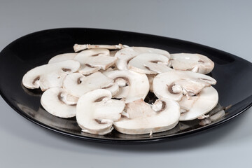 Sliced raw button mushrooms on black dish close-up