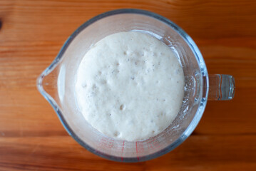 Rising artisan dough in glass bowl, fresh bread preparation, handmade sourdough proofing, homemade bread concept