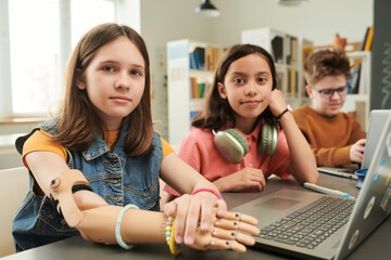 Colorful portrait of children using computers in school library and looking at camera focus on young girl with arm prosthetic