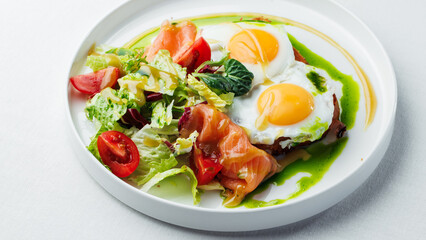 Breakfast, two eggs served on toasted bread with a green herb sauce. Accompanied fresh salad, cherry tomatoes, and smoked salmon slices, all elegantly presented on a white plate and white background