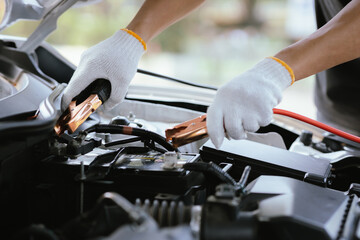 A male motor mechanic stands in a workshop, performing a safety inspection on a car engine....