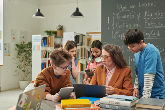 Colorful portrait of diverse group of children talking to female teacher during computer class in school library copy space