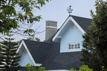 A house with a blue roof and a weather vane on top. roof shingle and wooden garret house.